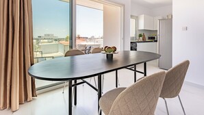 Ein moderner Essbereich mit großem Tisch und Stühlen, Blick auf die Stadt durch große Fenster, und eine Küche im Hintergrund.