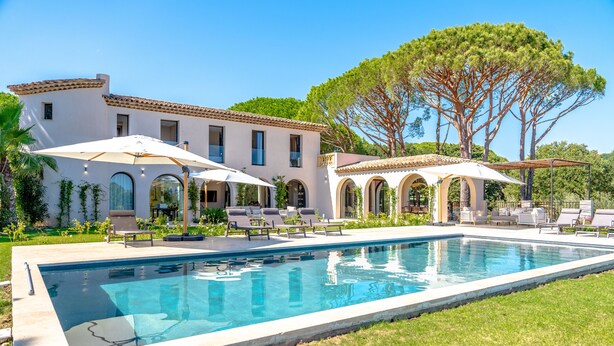A pool with lounge chairs and umbrellas, a large tree, and a building with arches. - Magnificient Villa totally renovated in 2023 with sea view and Saint Tropez   (Grimaud)