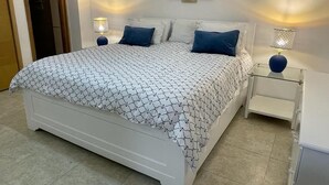 A bedroom with a bed, two bedside lamps, a wall-mounted artwork, and a door. - Amazing 2BR Beach Apartment with Ocean View for 6 (Playa Juan Dolio)