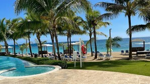 A pool area with lounge chairs and palm trees, overlooking the ocean. - Amazing 2BR Beach Apartment with Ocean View for 6 (Playa Juan Dolio)