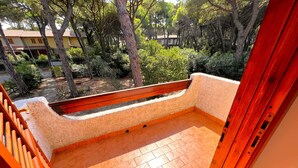 A balcony with a tiled floor, a wooden railing, and a view of trees and buildings.