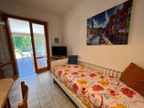 A bedroom with a bed, a TV, a chair, a table, and a painting on the wall. - Delfini (Grosseto)