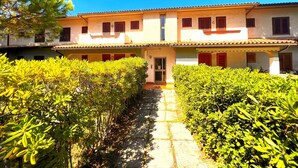 A two-story building with a tiled roof, a central entrance, and a garden with trimmed bushes.