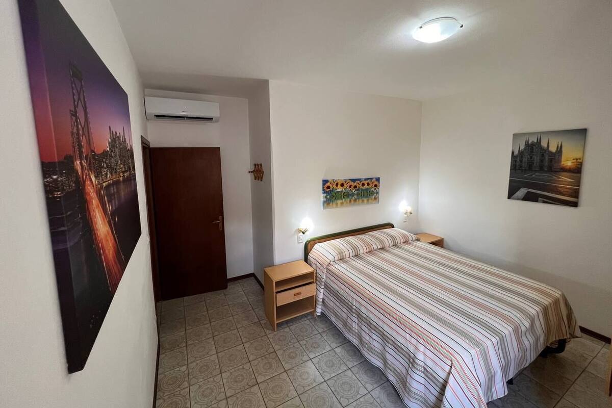 A bedroom with a bed, a nightstand, a wall-mounted air conditioner, and two paintings.