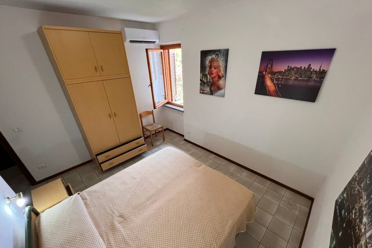 A bedroom with a bed, wardrobe, window, and two wall-mounted pictures.