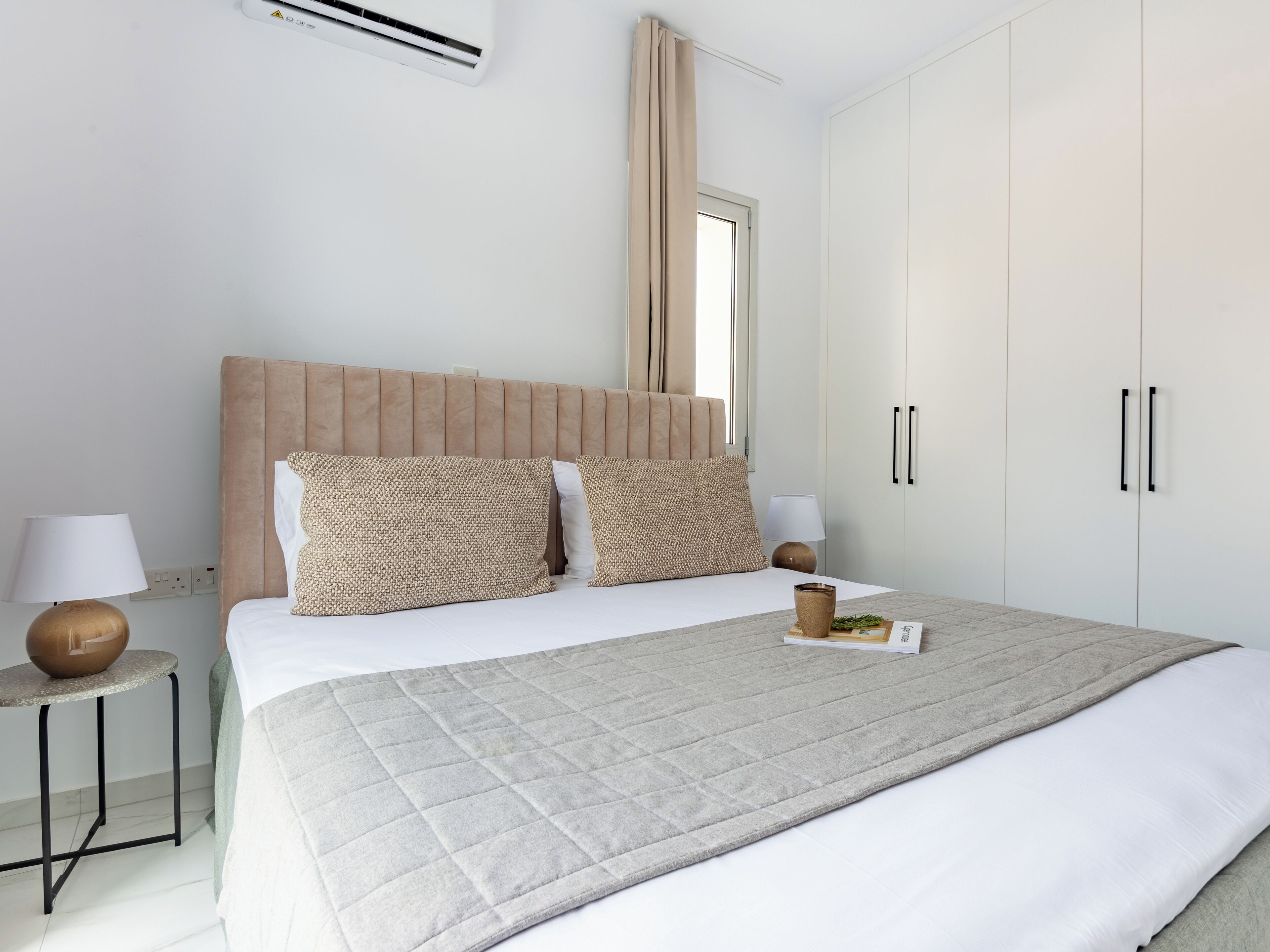 A bedroom with a bed, bedside tables, a wardrobe, and an air conditioning unit.