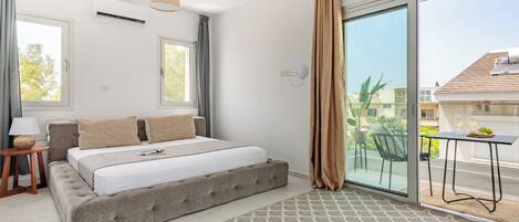 Un dormitorio moderno con una cama grande, una mesita de noche, una lámpara y vistas al balcón exterior.