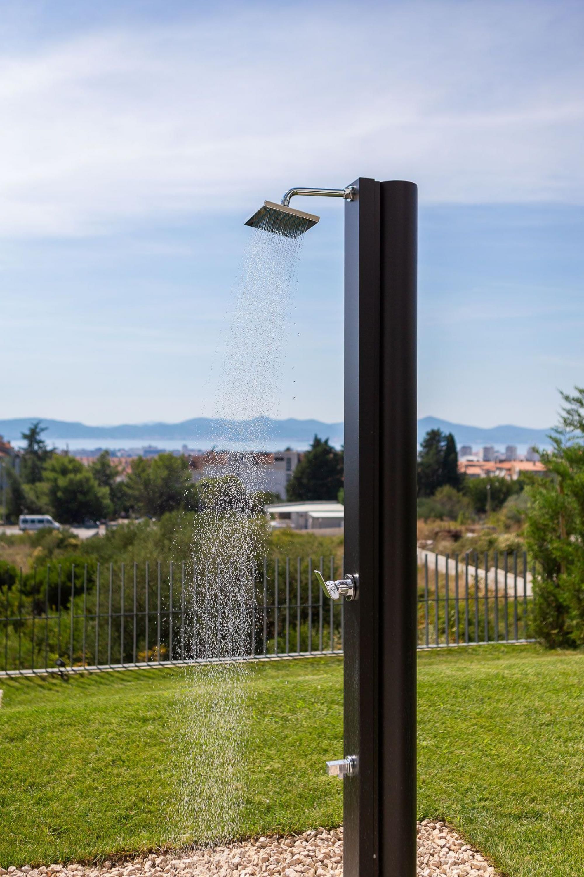 A modern outdoor shower with a clear view of a distant cityscape and mountains.