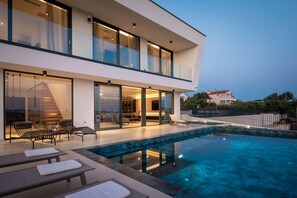 Une maison moderne à deux étages, dotée d’une piscine, d’un espace extérieur aménagé et d’un escalier menant à l’étage supérieur.