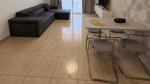 Una sala de estar moderna con un sofá seccional, una mesa de comedor con sillas, un televisor de pantalla plana y un amplio ventanal con cortinas.