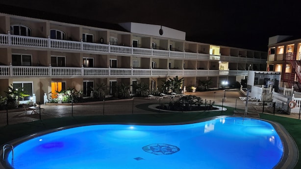 Una piscina con diseño circular, rodeada por una cerca, y un edificio de varios pisos con balcones al fondo.