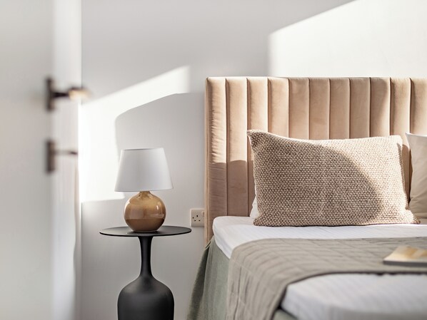 A bedroom with a bed, a bedside table with a lamp, and a window.