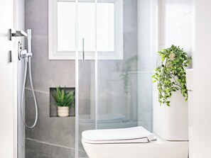 A modern bathroom with a glass shower enclosure, a white toilet, and a potted plant.