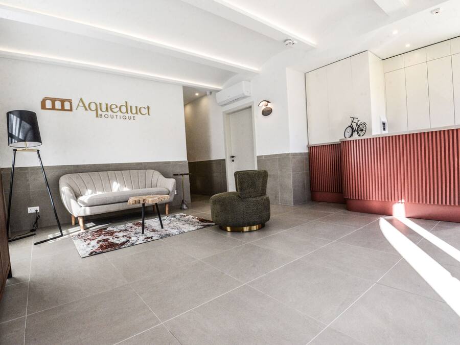 Um lobby moderno com um sofá, uma poltrona, um balcão de recepção e uma placa fixada na parede.