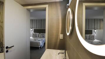 A modern bathroom with a large mirror, a sink, and a door leading to a bedroom.