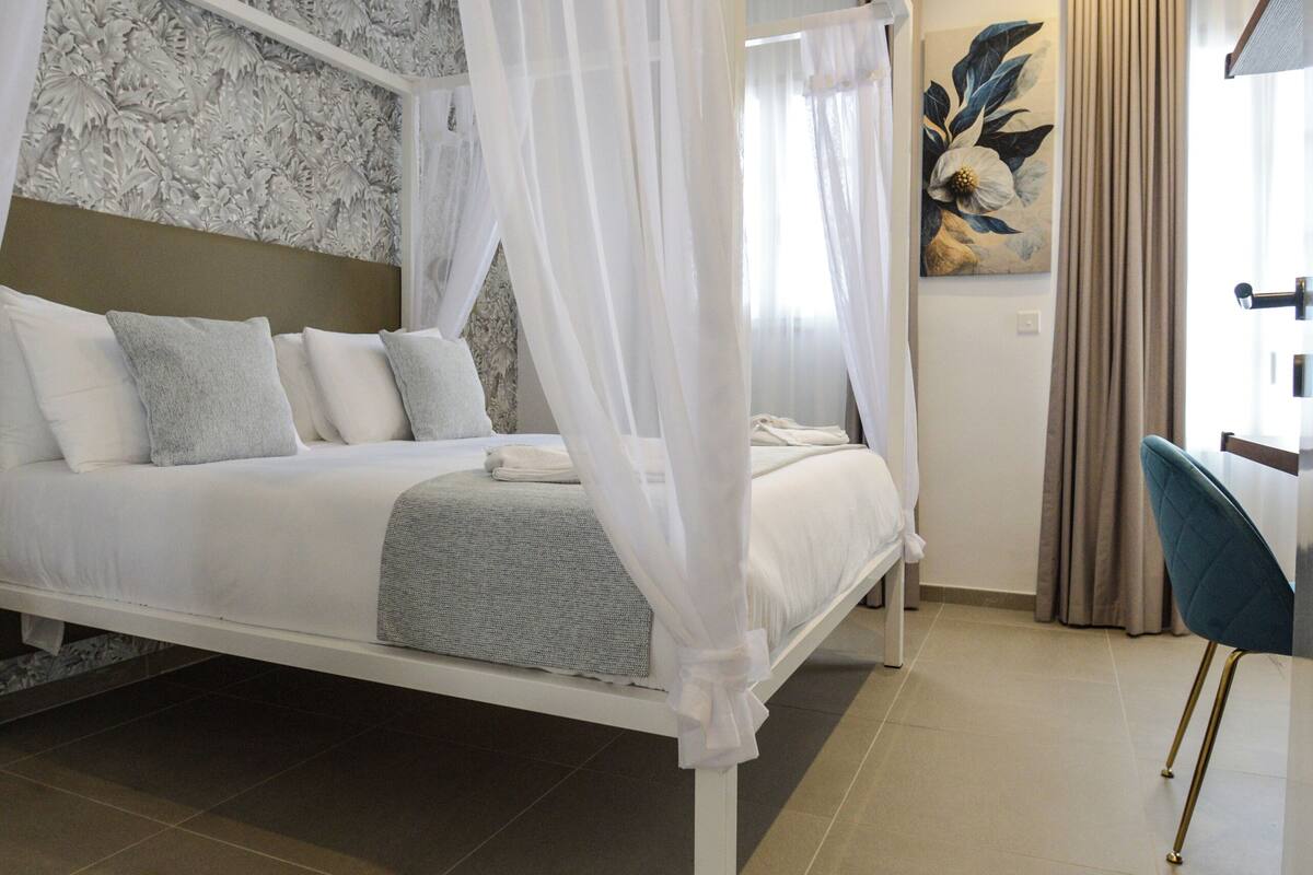 A modern bedroom with a four-poster bed, a desk, and a chair.