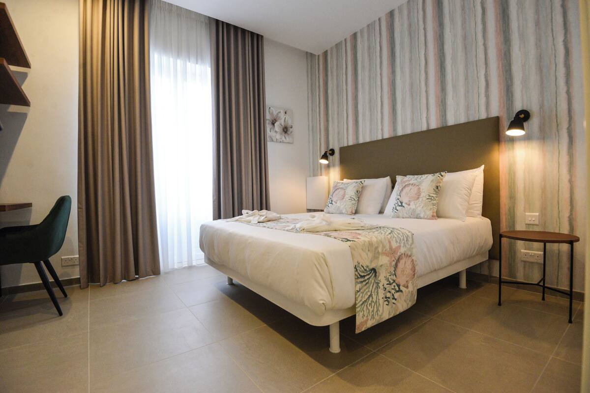 A bedroom with a large bed, a chair, a bedside table, and curtains.