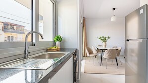 Ett modernt kök med ett kylskåp i rostfritt stål, en diskho med blandare och en matplats med stolar och ett bord.