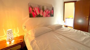 A hotel room with a bed, a nightstand, a lamp, and a painting of pink tulips on the wall. - Paguro (Grosseto)