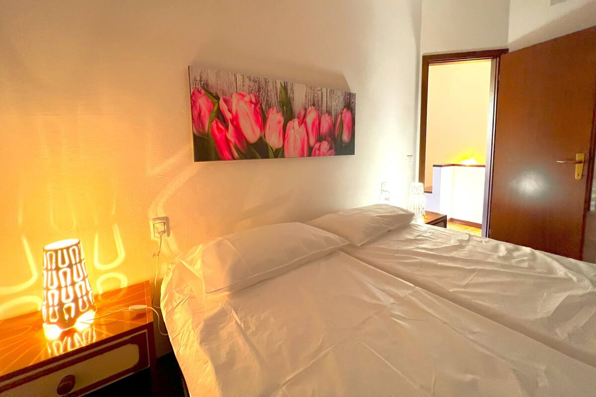 A hotel room with a bed, a nightstand, a lamp, and a painting of pink tulips on the wall.