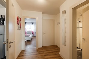 A hallway with wooden flooring, a door leading to a bathroom, and a refrigerator on the left.