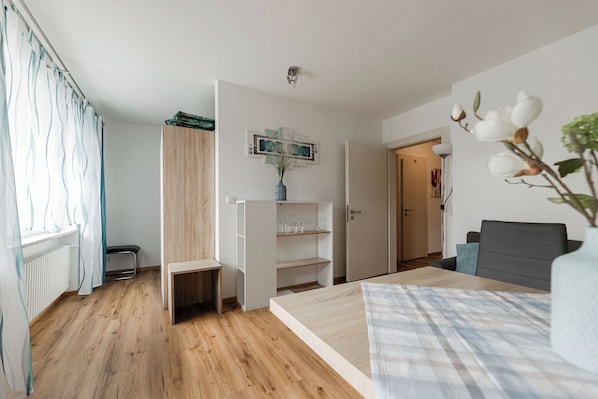 A room with a bed, a desk, a wardrobe, and a door leading to another room.