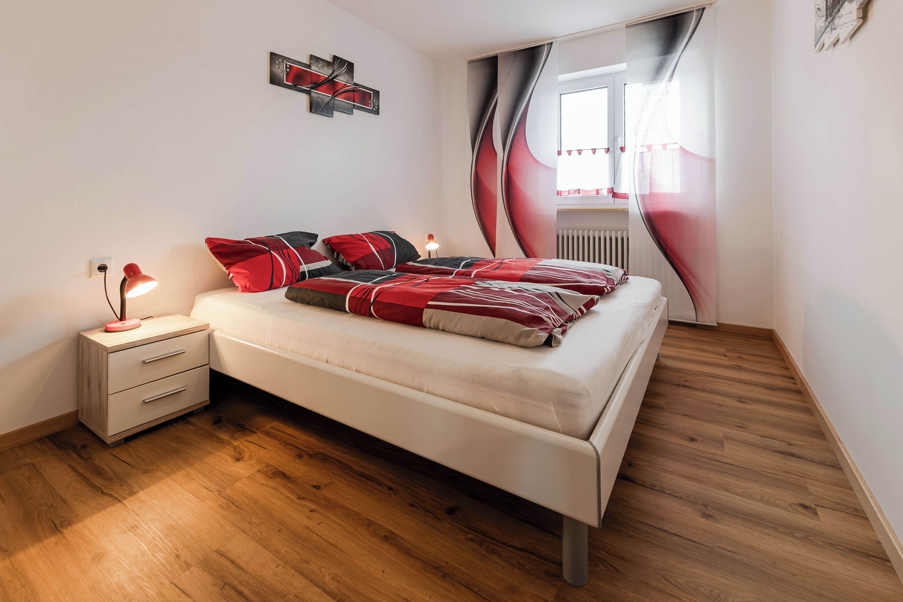 A bedroom with a bed, bedside table, lamp, and a window with curtains.