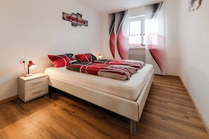 A bedroom with a bed, bedside table, lamp, and a window with curtains.