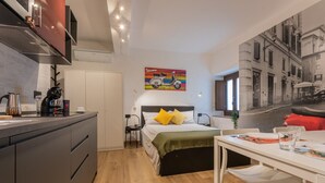 A compact hotel room with a kitchenette, a bed with yellow pillows, a dining area, and a cityscape painting on the wall. - Special 10 apartment by Wonderful Italy (Torino)