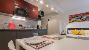 A modern kitchen with a microwave, stove, and sink. There is a dining table with plates and glasses. A bed with pillows is visible in the background. - Special 10 apartment by Wonderful Italy (Torino)