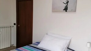 A bedroom with a striped bedspread, a white pillow, a door, a radiator, and a wall with a black and white artwork.