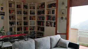 A living room with a grey sofa, a dining table with chairs, and a bookshelf filled with books.