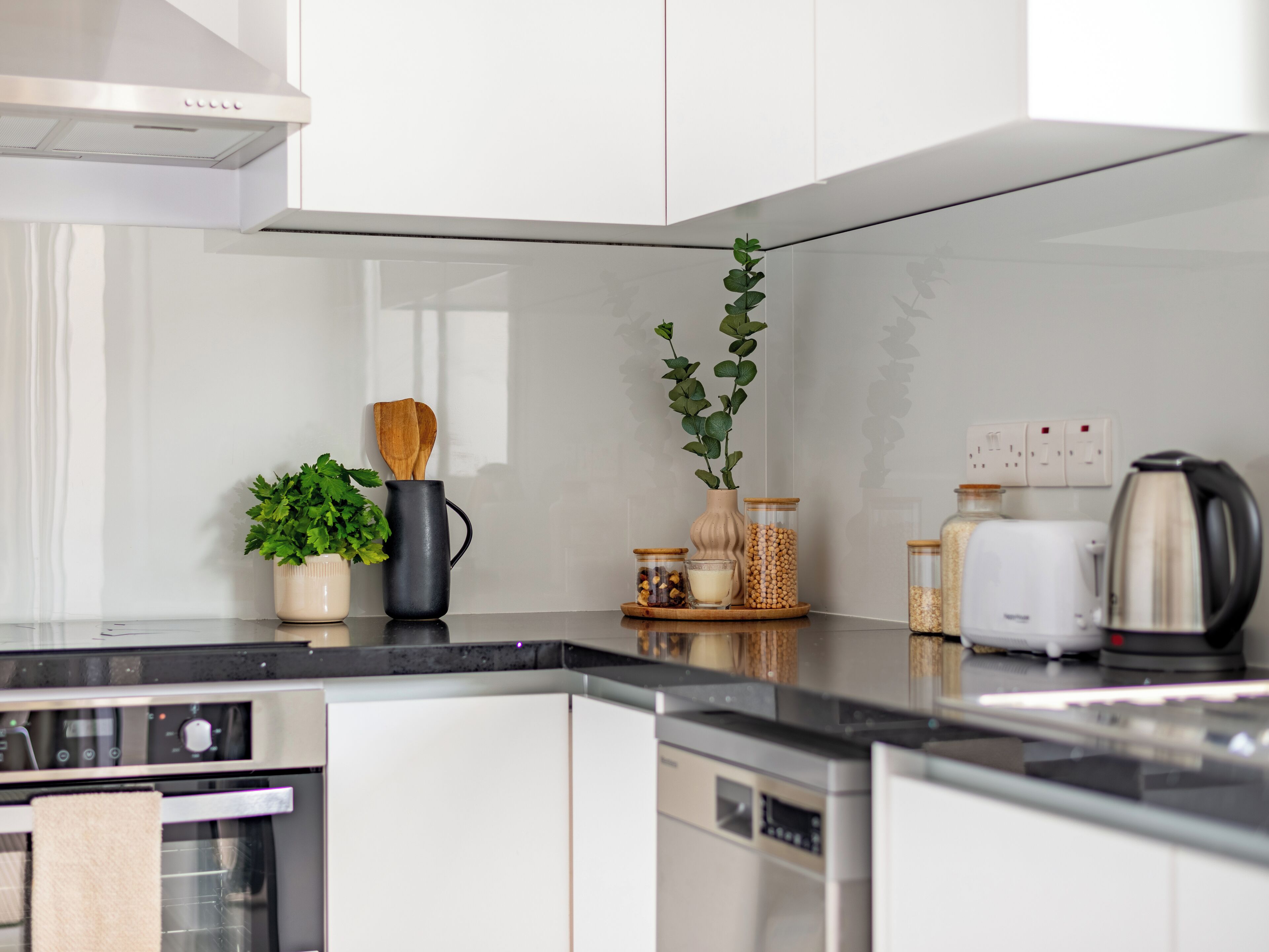 A modern kitchen with white cabinets, a black countertop, a stove, an oven, a dishwasher, and various kitchen appliances and utensils.
