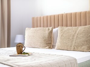A neatly made bed with a beige headboard, two pillows, a small decorative mug, and a book on a white bedspread. - Sanders Cruise - Bright 2-bdr Apt With 2 Balconies (Limassol)