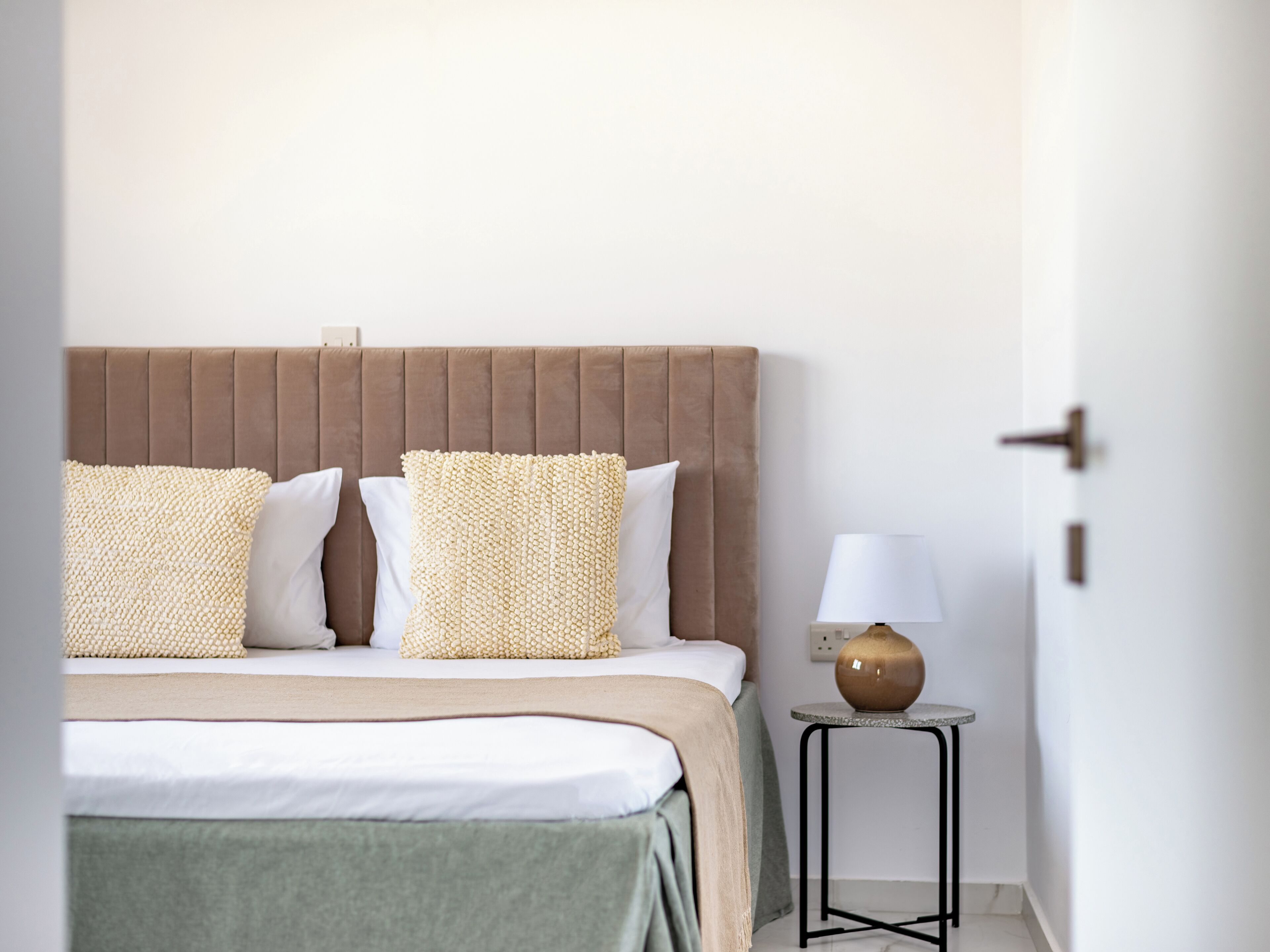 A neatly made bed with a brown headboard, two textured pillows, and a bedside table with a lamp.