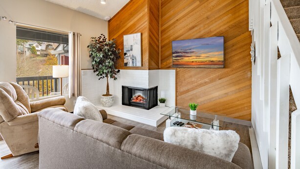 Ein modernes Wohnzimmer mit Kamin, einer Couch, einem Couchtisch und Blick ins Freie.