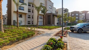 A residential building with multiple balconies, a paved walkway, and a parked car. - Prime Select New Giza (6th of October City)
