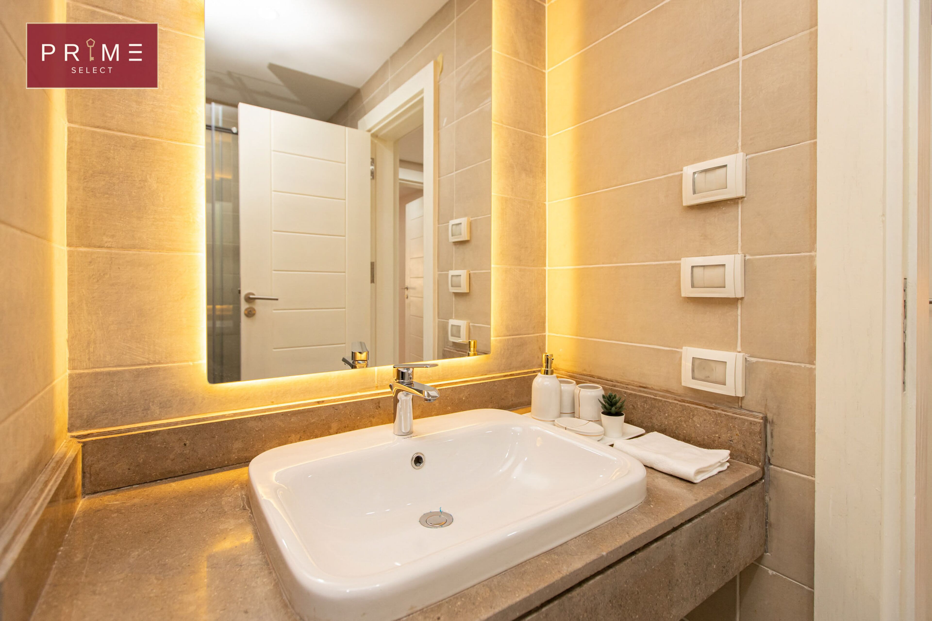 A modern bathroom with a large white sink, a mirror, and beige tiles.