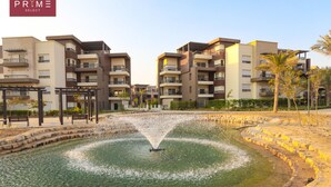 A residential complex with multiple apartment buildings, a central water feature, and a well-maintained garden area. - Prime Select New Giza (6th of October City)