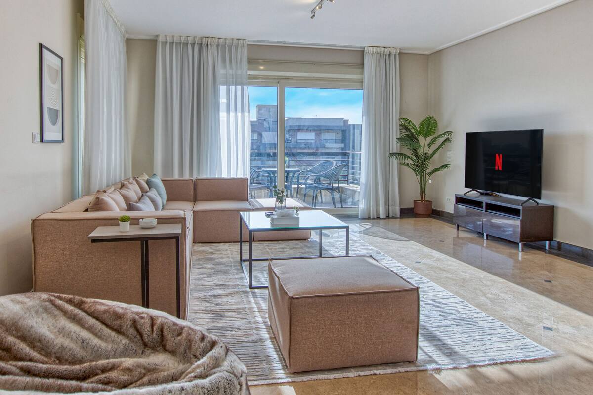 A modern living room with a sofa, ottoman, coffee table, and a flat-screen TV.
