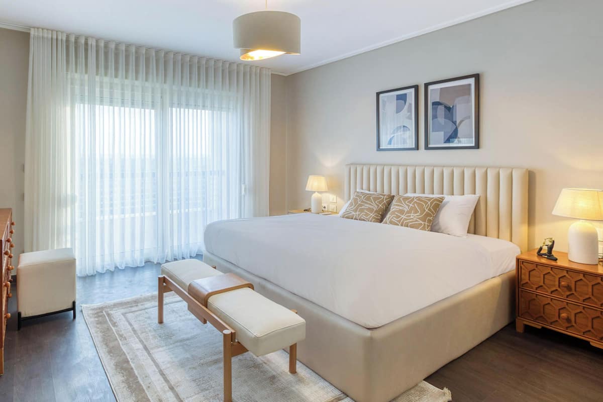 A modern hotel room with a large bed, bedside tables, a bench, and a dresser.
