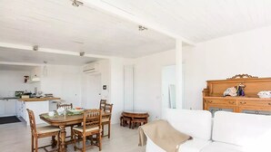 Zona d'estar àmplia amb taula de dinar, cadires de fusta, sofà blanc i un armari de fusta.