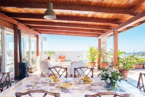 A covered outdoor dining area with wooden beams, a tiled floor, and potted plants.