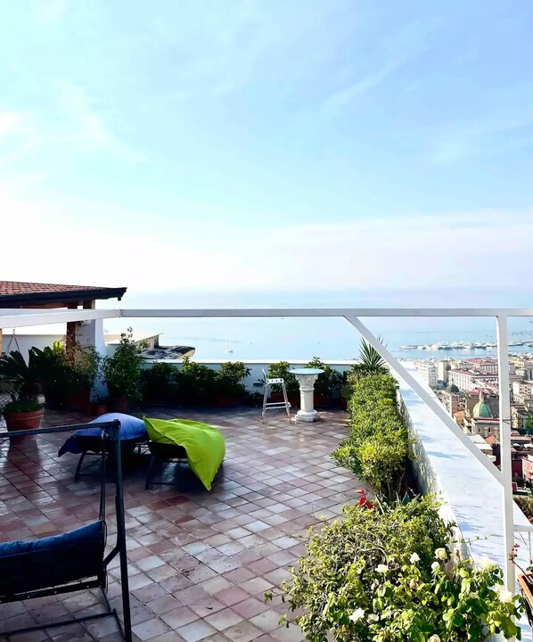 A terrace with a view of the sea, potted plants, and outdoor furniture.