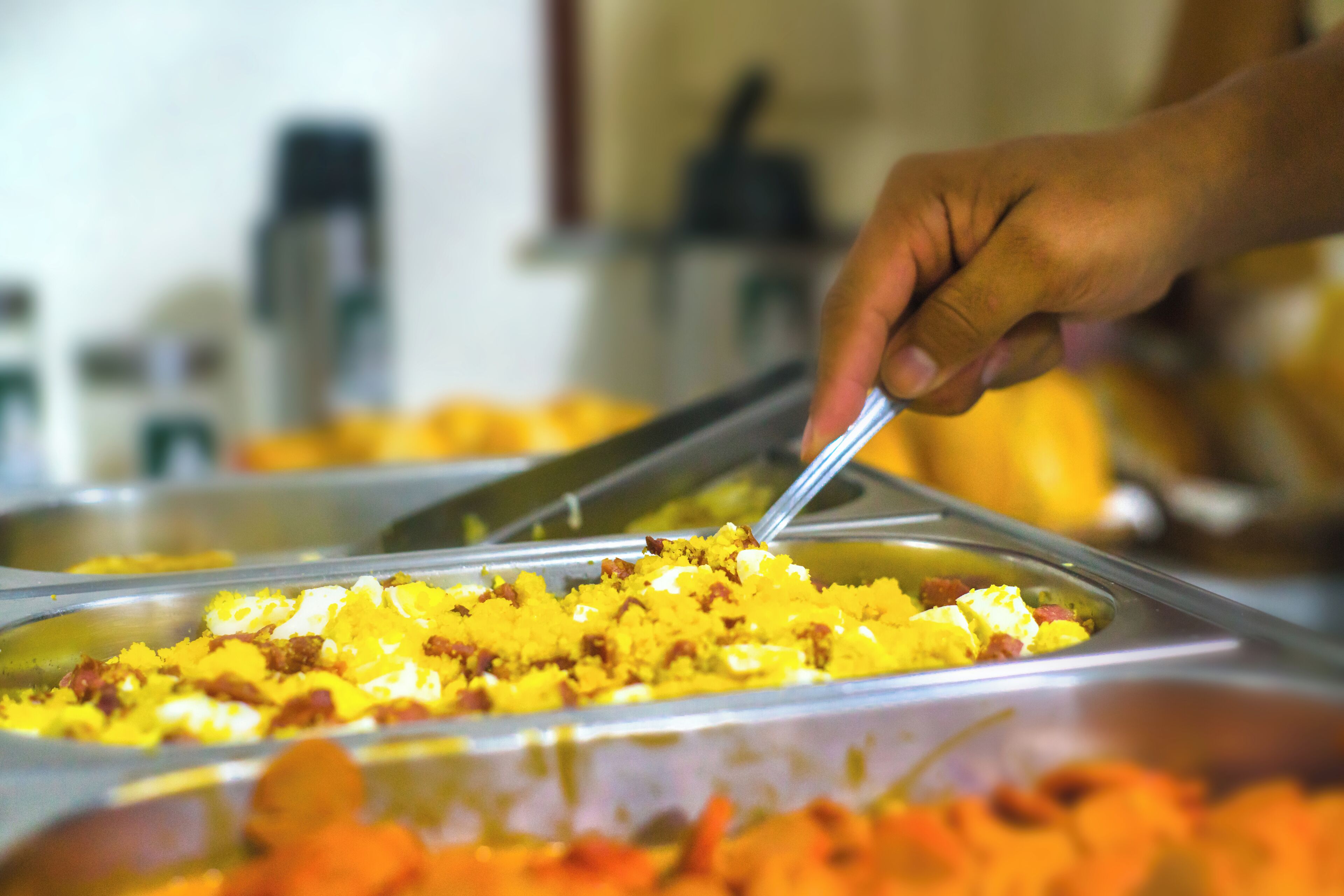A hand using tongs to serve food from a buffet tray.