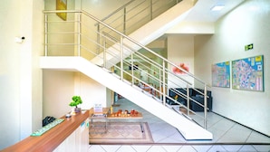 A reception area with a wooden counter, a small plant, and a table with various items. A staircase with a metal railing leads to an upper level. - Hotel Pinheiro (Ibiapina)