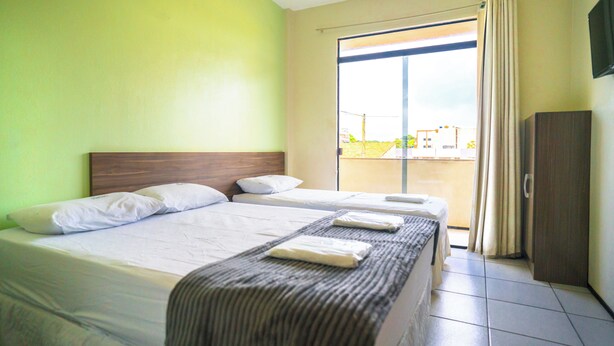 A hotel room with two beds, a large window with curtains, and a view of the outside. - Hotel Pinheiro (Ibiapina)