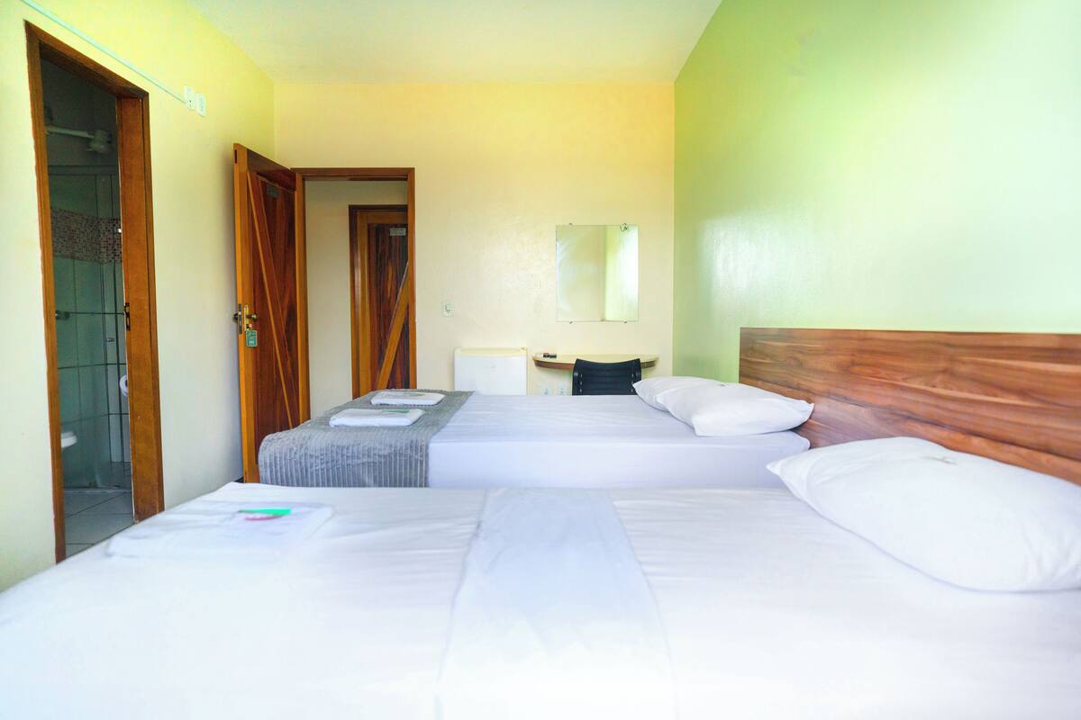 A hotel room with two beds, a wooden headboard, a small desk, and a mirror on the wall.