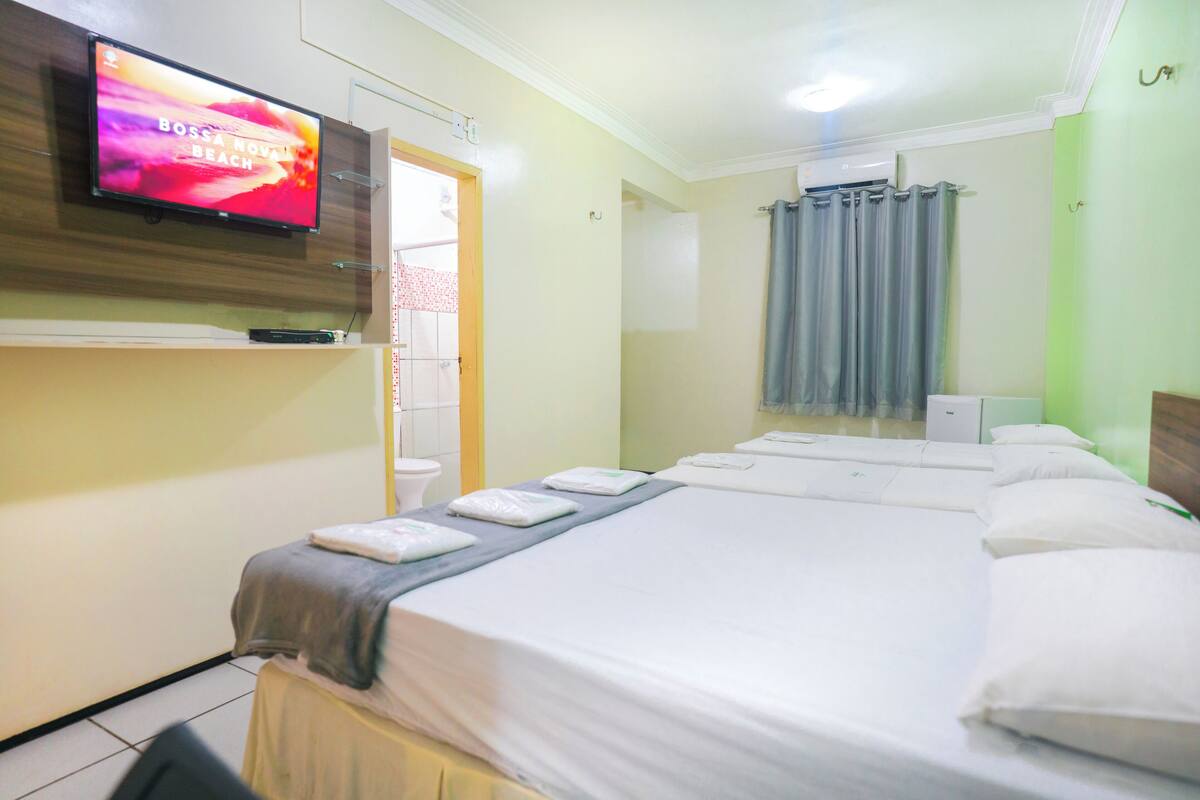 A hotel room with a bed, a television mounted on the wall, and a bathroom visible through an open door.