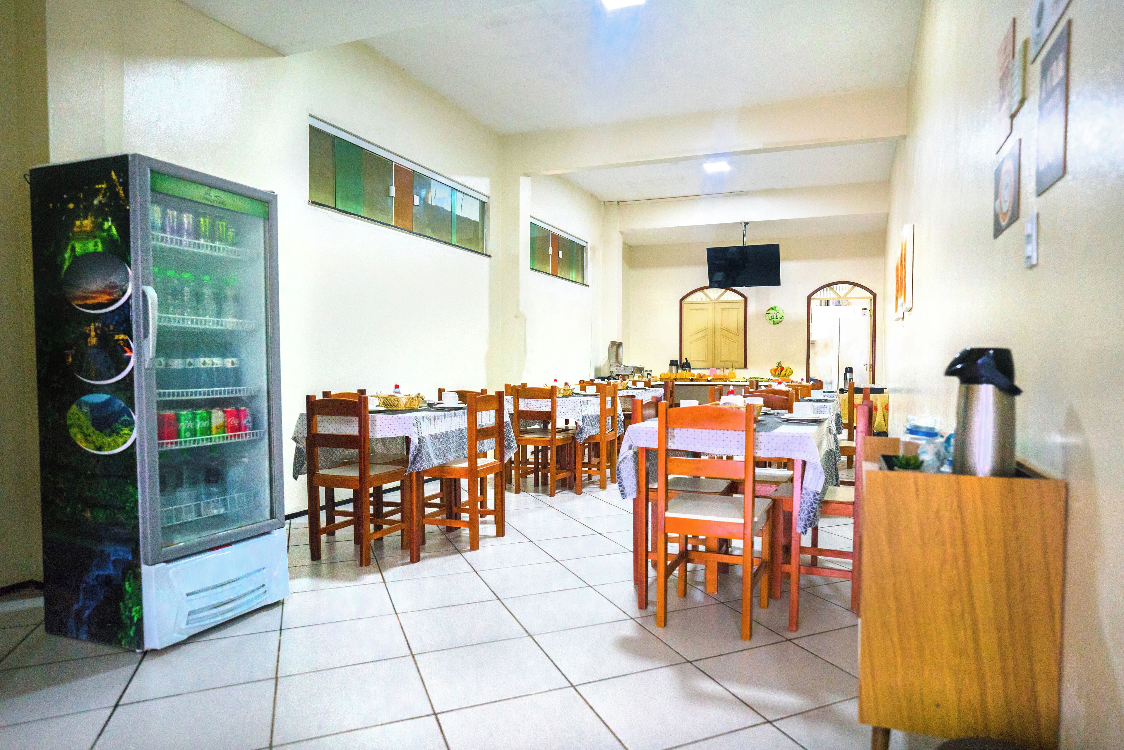 A dining area with tables and chairs, a refrigerator, and a television on the wall.